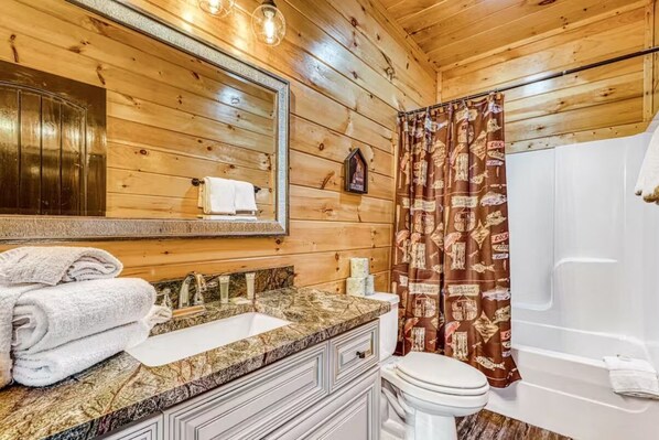 Baño de cabaña de madera con lavamanos, espejo, inodoro y cortina de ducha.