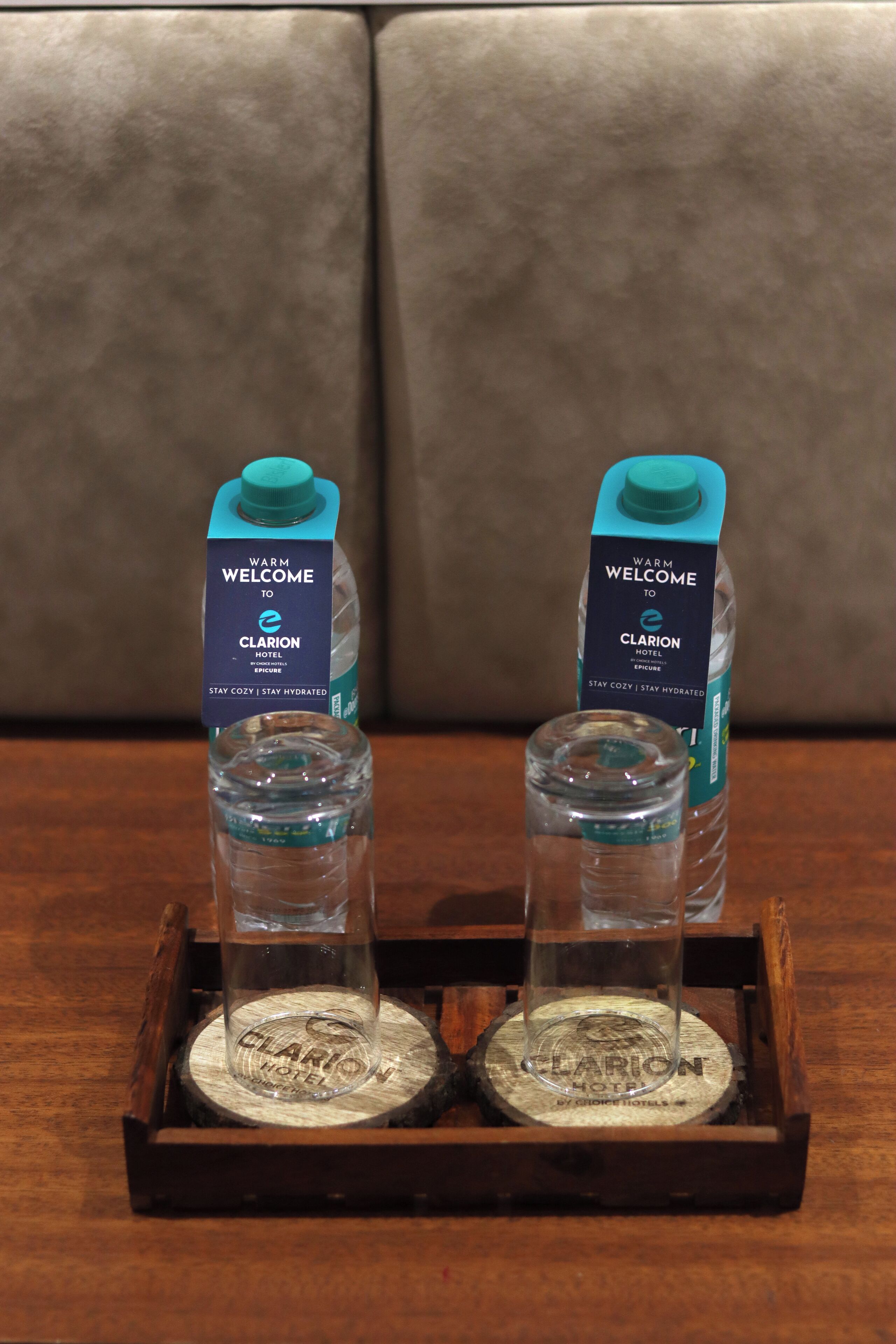 Two water bottles with 'Warm Welcome to Clarion Hotel' labels on a wooden coaster tray.