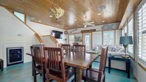 Ein geräumiges Zimmer mit Holzbalkendecke, einem Esstisch mit Stühlen, einem Sofa und einer Lampe.
