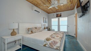 Ein Schlafzimmer mit Holzboden, einem Bett mit floralem Bettzeug, einem Nachttisch mit Lampe und einer wandmontierten Klimaanlage.