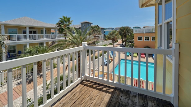 Ein Balkon mit Holzboden, der einen Blick auf einen Swimmingpool und einen Strand bietet.