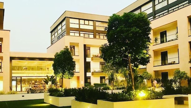 Un bâtiment moderne à plusieurs étages, doté d’un espace extérieur aménagé pour s’asseoir et d’un espace vert bien entretenu.