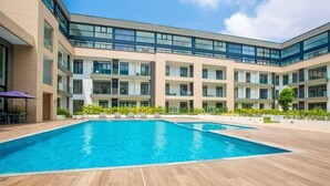 Un bâtiment moderne doté d’une piscine, de plusieurs balcons et offrant une vue sur un ciel dégagé.