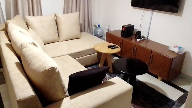 Un salon avec un canapé beige, une petite table ronde, un téléviseur fixé au mur et un meuble en bois.