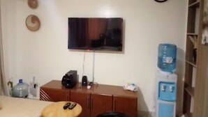 Un salon avec un téléviseur à écran plat fixé au mur, un meuble en bois en dessous et un distributeur d’eau sur la droite.