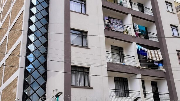 Ein mehrstöckiges Wohngebäude mit Balkonen, einem Auto in der Garage und einer auffälligen Fassade mit einem fensterartigen Muster.