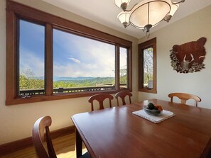 A dining area with a large table, four chairs, and a view of mountains through large windows. - Bear Necessities - 2BR, sleeps up to 6, amazing view, hot tub + free Biltmore tix (Sylva)