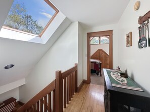 A room with a sloped ceiling, wooden railing, a table with a decorative cloth, and a view through a window. - Bear Necessities - 2BR, sleeps up to 6, amazing view, hot tub + free Biltmore tix (Sylva)