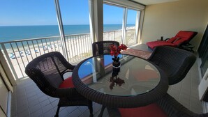 A balcony with a glass table and wicker chairs, overlooking a beach with umbrellas. - WATCH THE DOLPHINS PLAY FROM THE BALCONY! (Orange Beach)