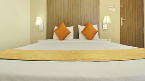 A hotel room with a large bed, two pillows, two wall-mounted lamps, a wooden door, and a light switch on the wall. - Ranas Residency (Tiruchirappalli)