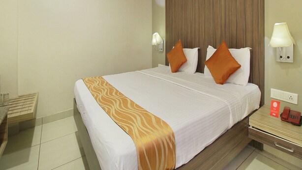 A hotel room with a bed, a nightstand, a telephone, and a wall-mounted lamp. - Ranas Residency (Tiruchirappalli)