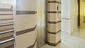 A hallway with a modern elevator, a glass door, and a tiled floor. - Ranas Residency (Tiruchirappalli)