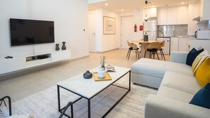Een moderne woonkamer met een flatscreen televisie, een salontafel en een bank met kussens.