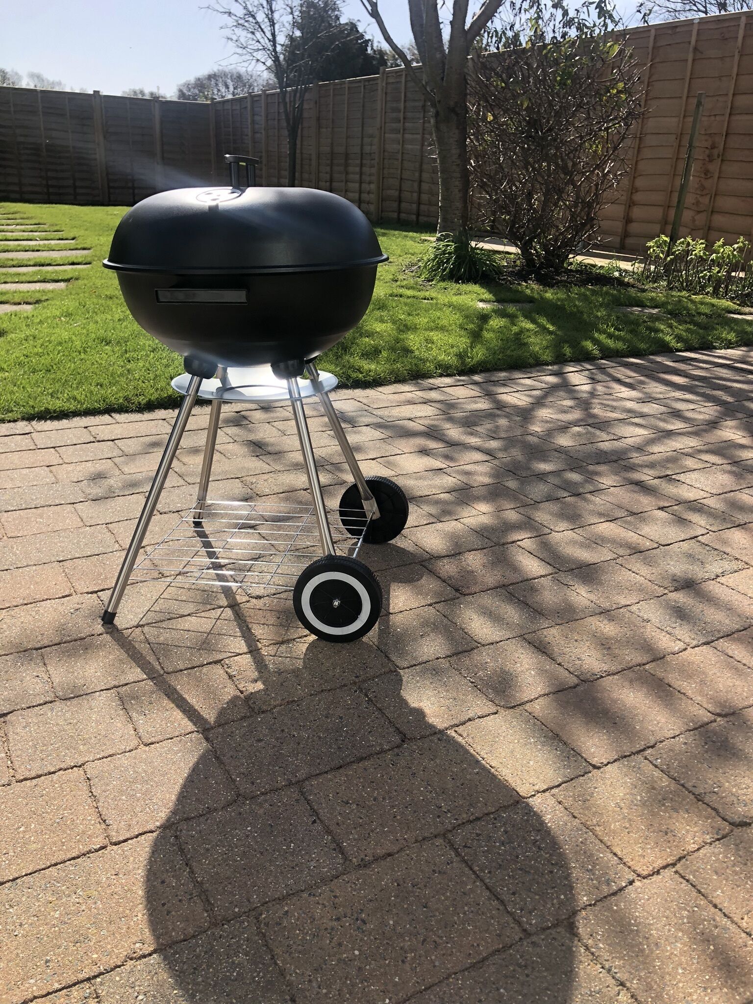 Ein schwarzer Grill mit Rollen auf einer gepflasterten Terrasse.