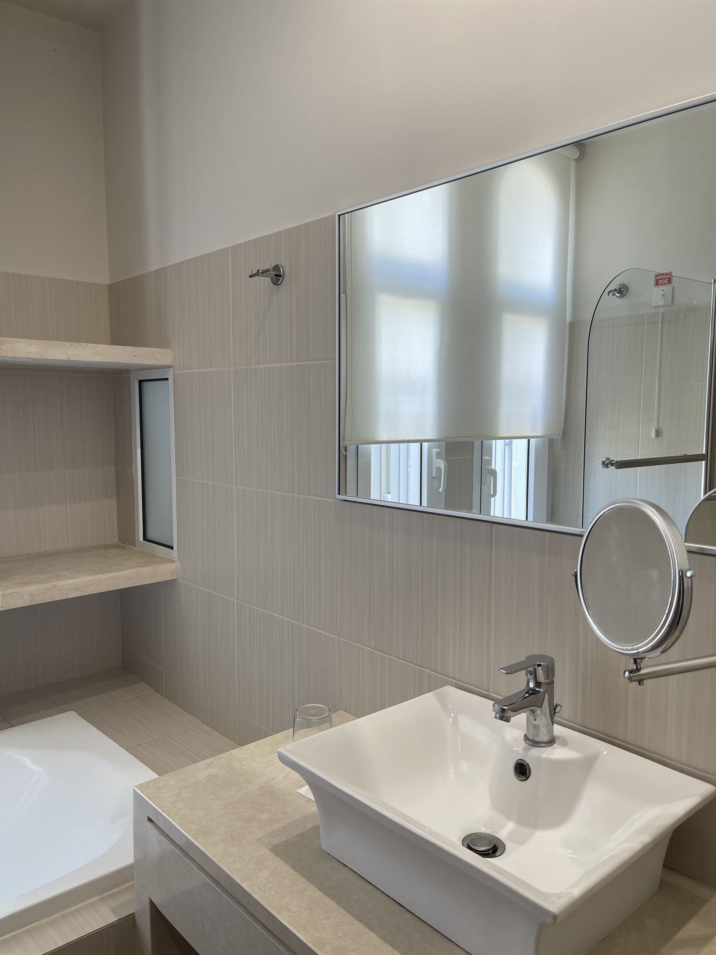 Un baño moderno con un lavamanos blanco, un espejo y una zona de ducha.