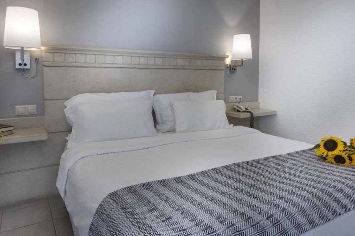 A hotel room with a bed, two bedside lamps, a telephone, and a decorative arrangement of sunflowers.