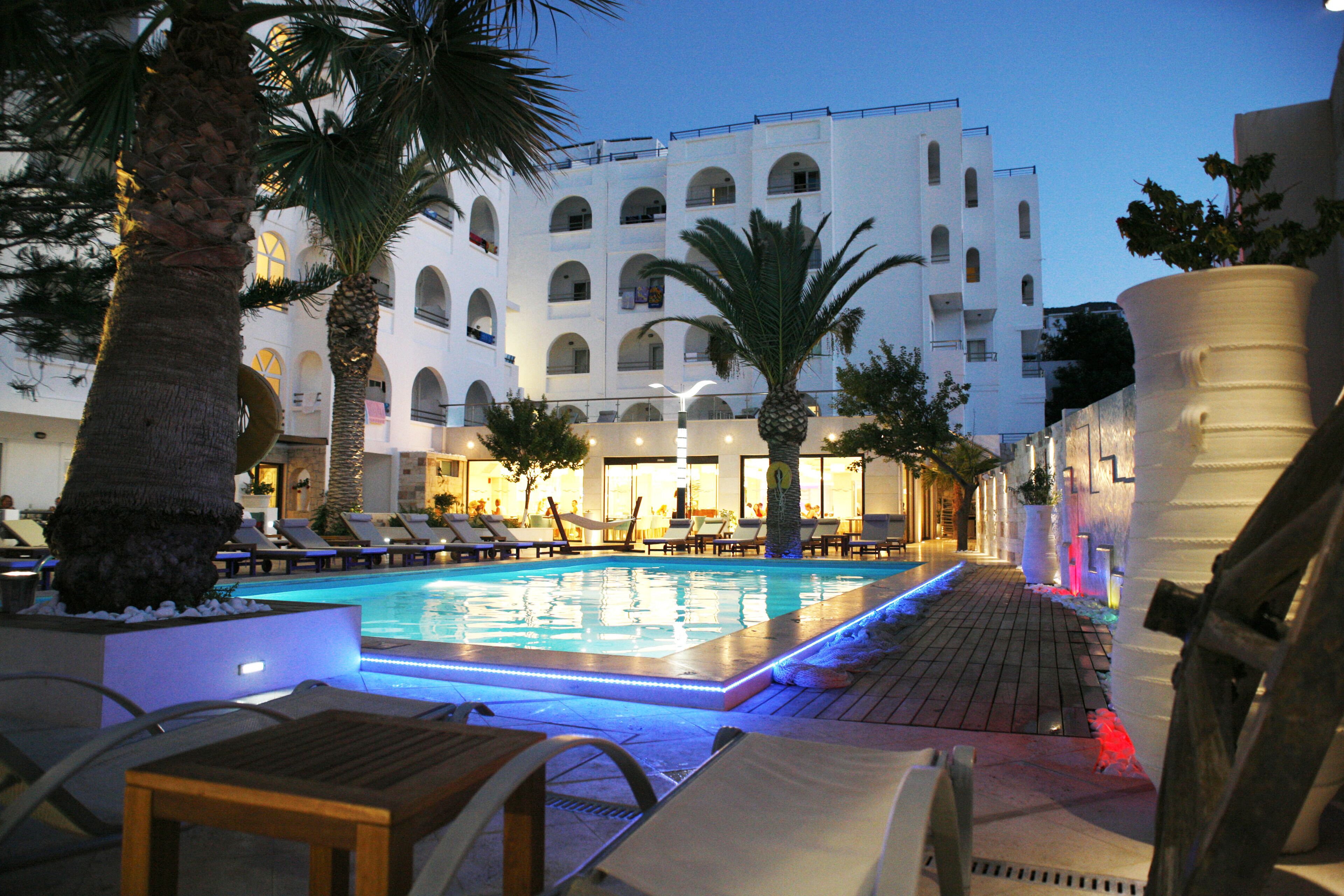 A pool area with lounge chairs and palm trees, surrounded by a white building with multiple balconies.