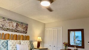 Una camera da letto con un letto, un comodino, una lampada, una cassettiera, uno specchio e una ventola a soffitto.