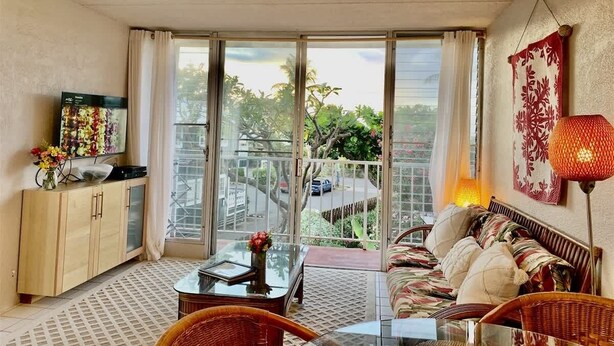 Una stanza con balcone, un divano, una TV, un armadio e una lampada.