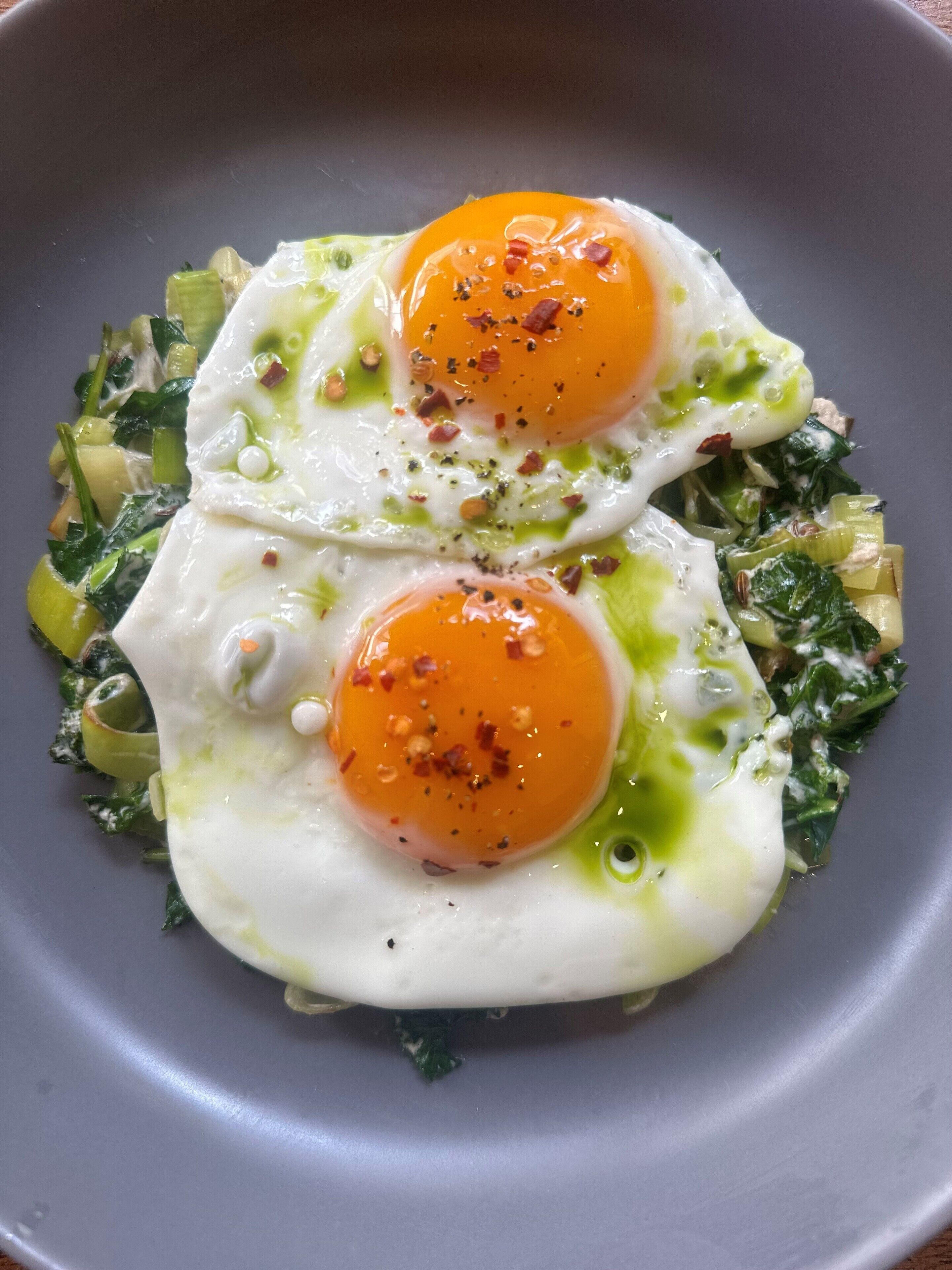 A plate with two sunny-side-up eggs, green vegetables, and a drizzle of sauce.