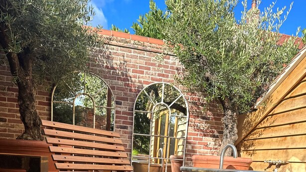 A wooden bench with a curved design, a brick wall, and a window with a metal frame. - NoTwenty9 Bar and Restaurant  (King's Lynn)