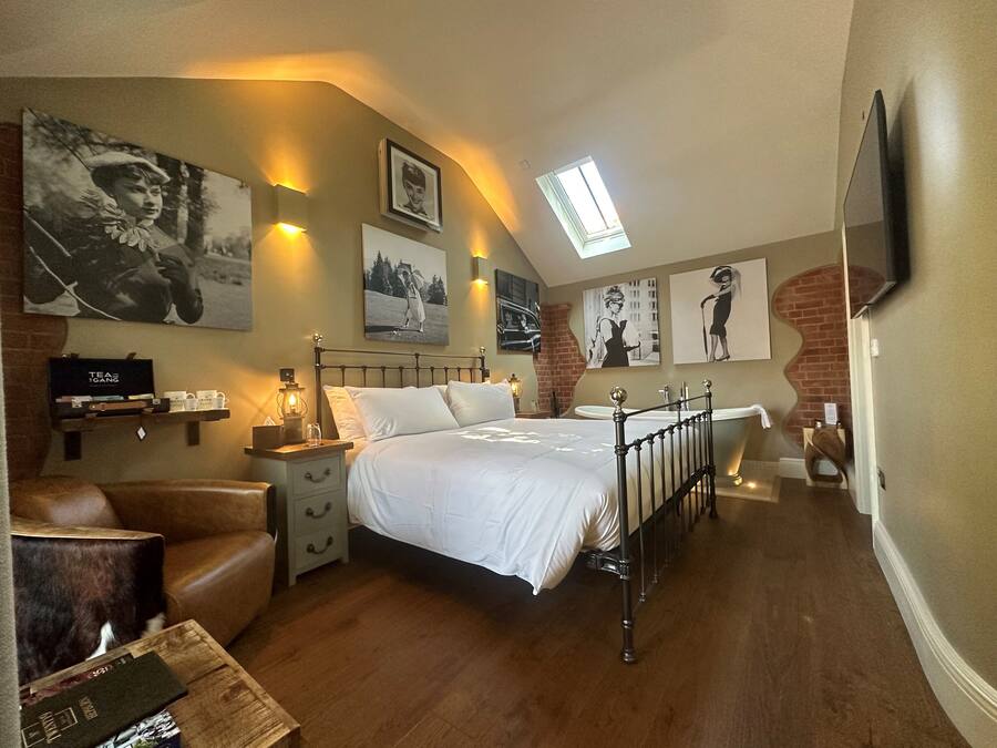 A bedroom with a bed, bedside tables, a nightstand, a chair, a small table with a box, and a wall-mounted TV.