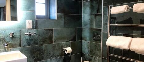 Une salle de bain moderne avec des carreaux de couleur sombre, un lavabo blanc, des toilettes et un porte-serviettes.