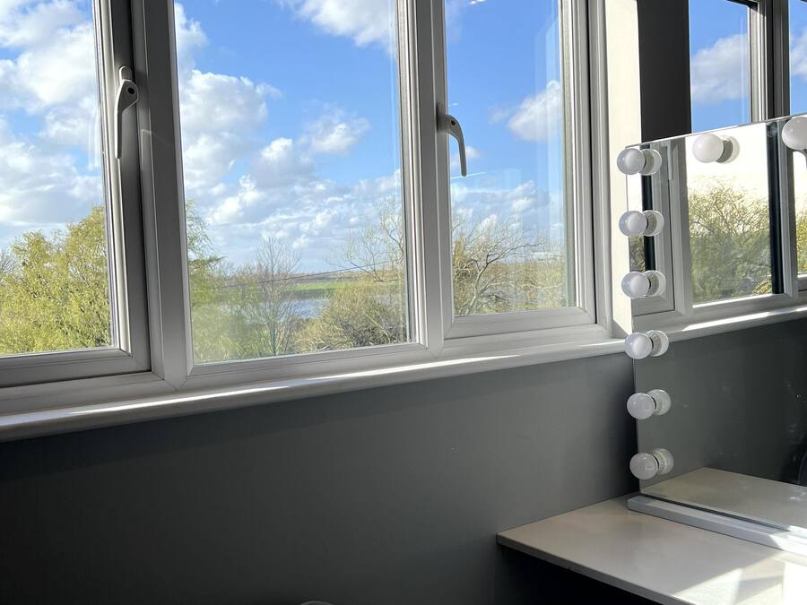 A room with large windows, a vanity with lights, and a chair.