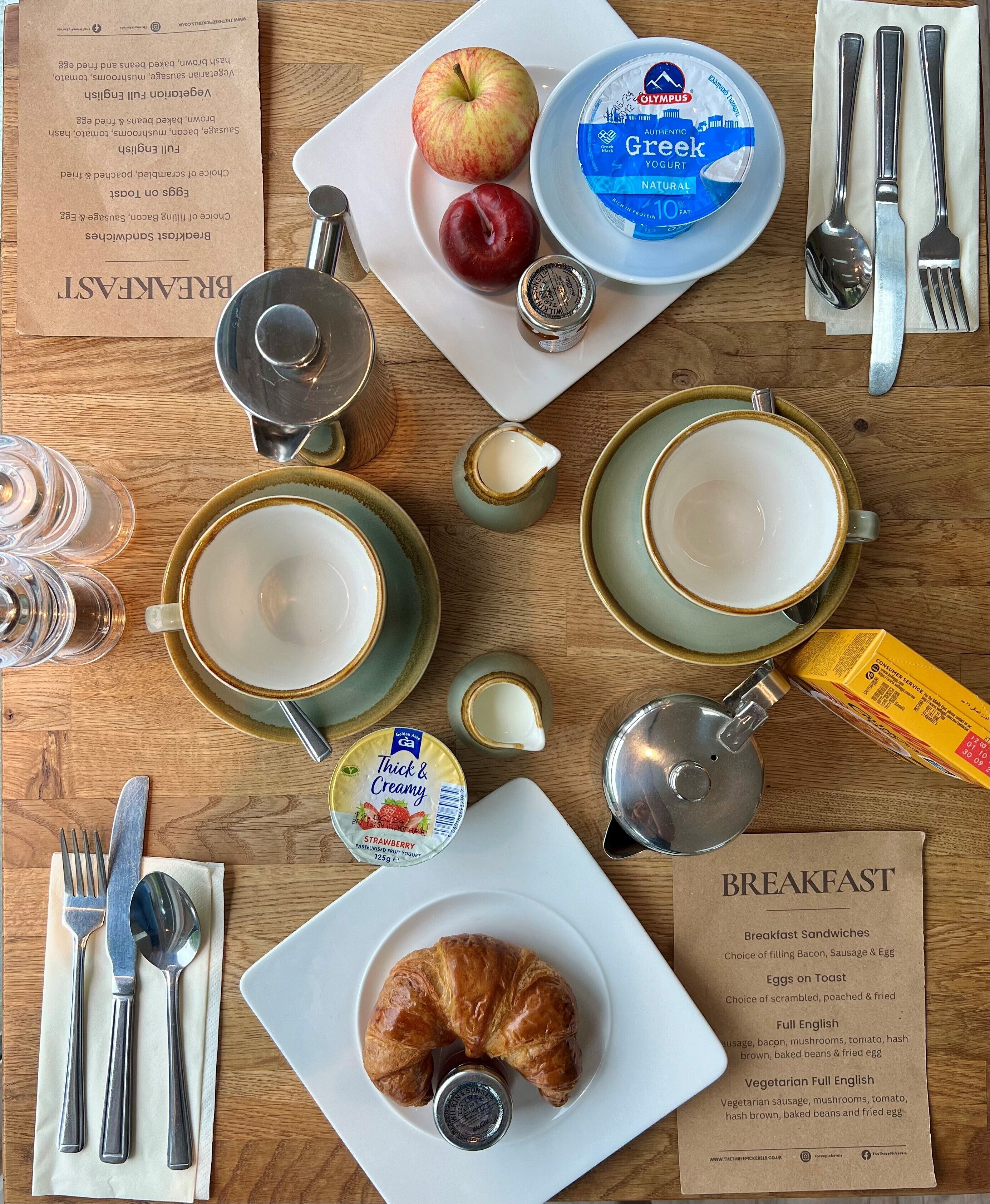 A breakfast setting with a croissant, yogurt, fruit, and a menu.