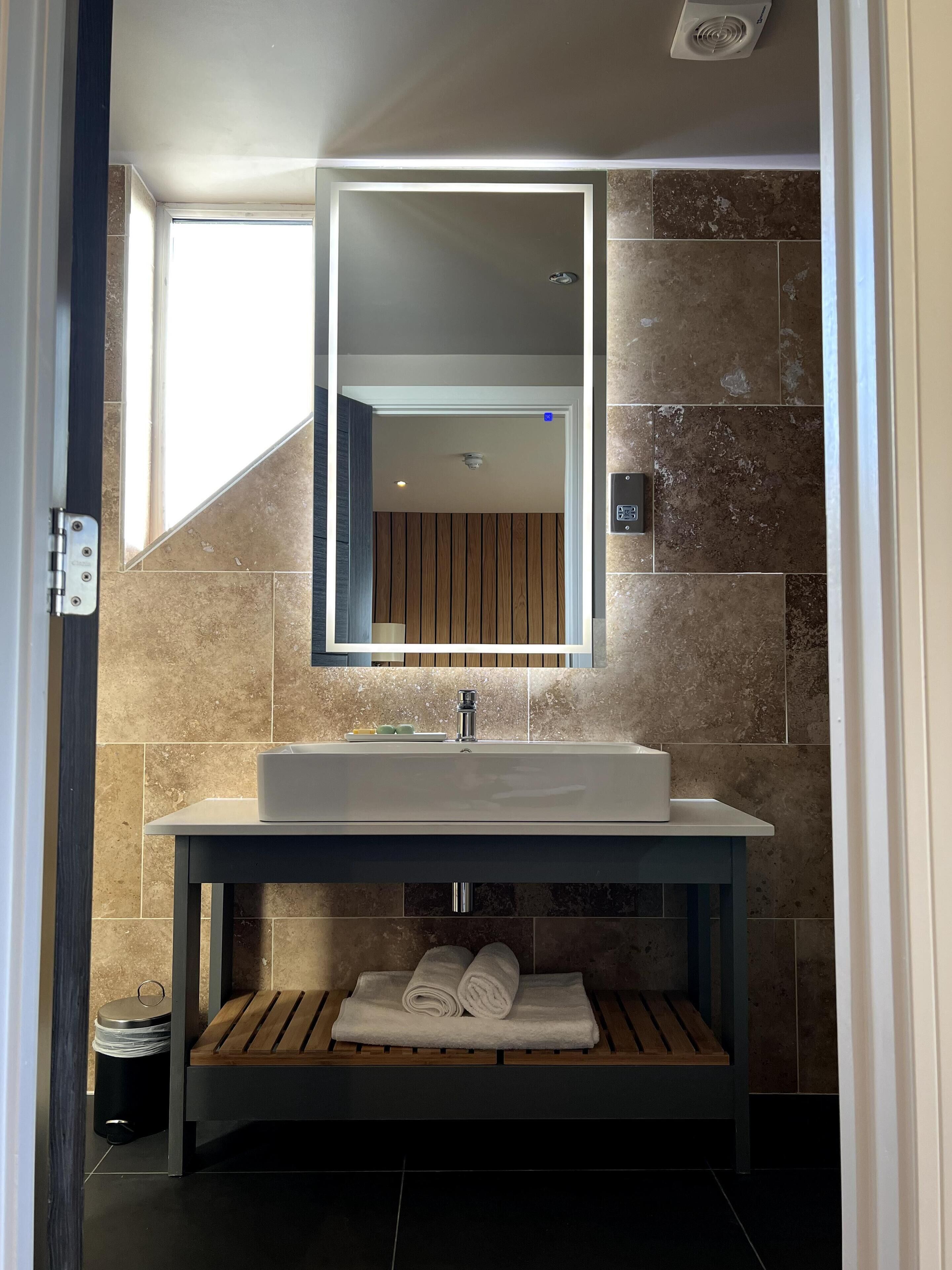 A modern bathroom with a large sink, wooden bench, and a mirror.