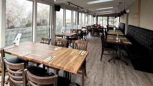 Un'ampia sala da pranzo con soffitti alti, grandi finestre e diverse possibilità di posti a sedere, tra cui tavoli e panche.
