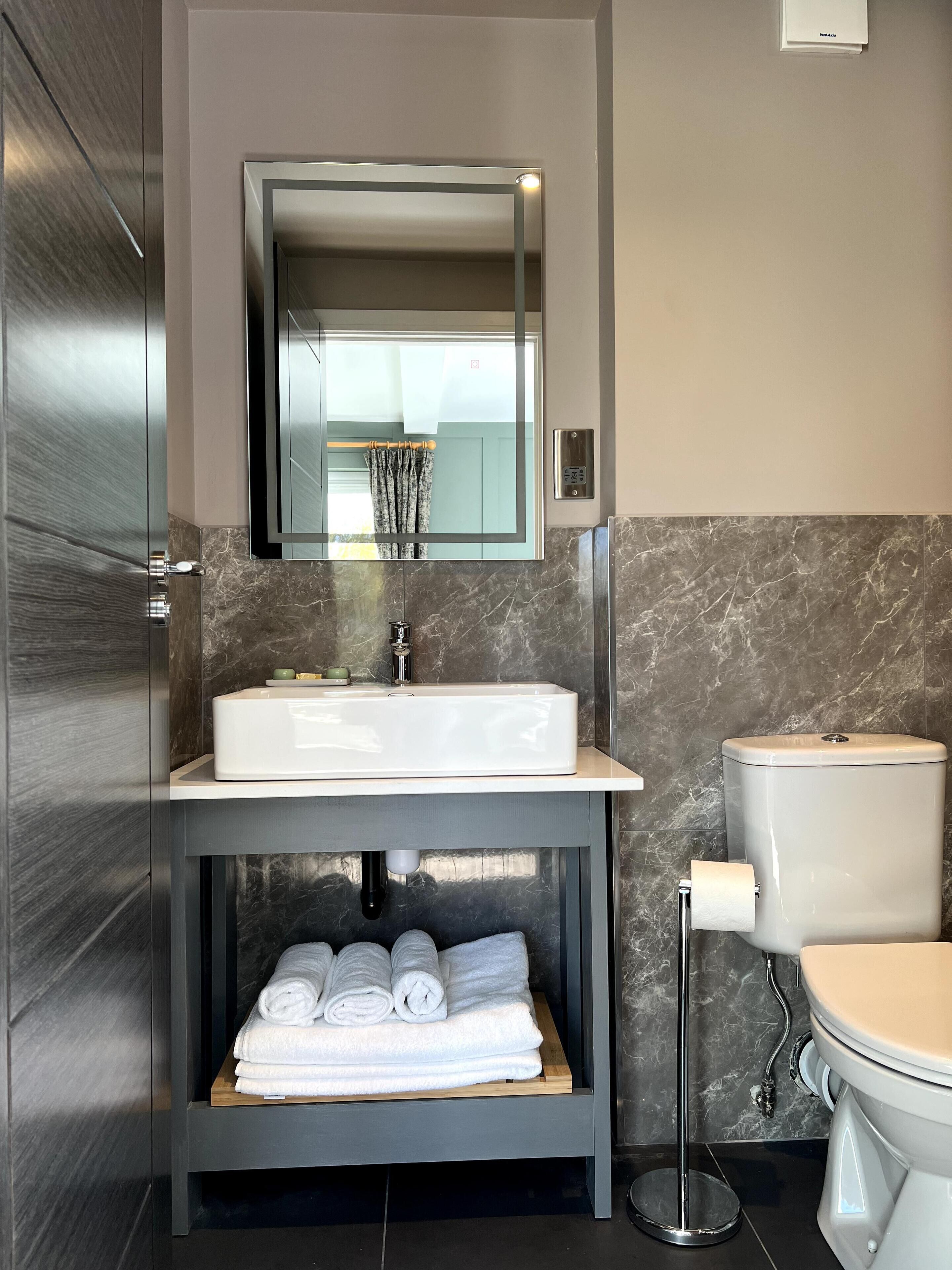 Een moderne badkamer met een inbouwwastafel, toilet en spiegel boven de wastafel.