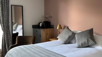 Una habitación de hotel moderna con una cama grande, un escritorio, una silla, un espejo y una mesita de noche con lámpara.