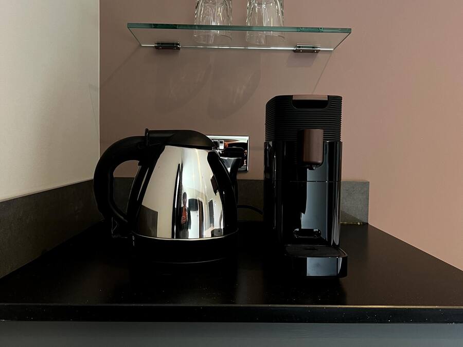 A coffee maker and a kettle on a black countertop with a glass shelf above them.
