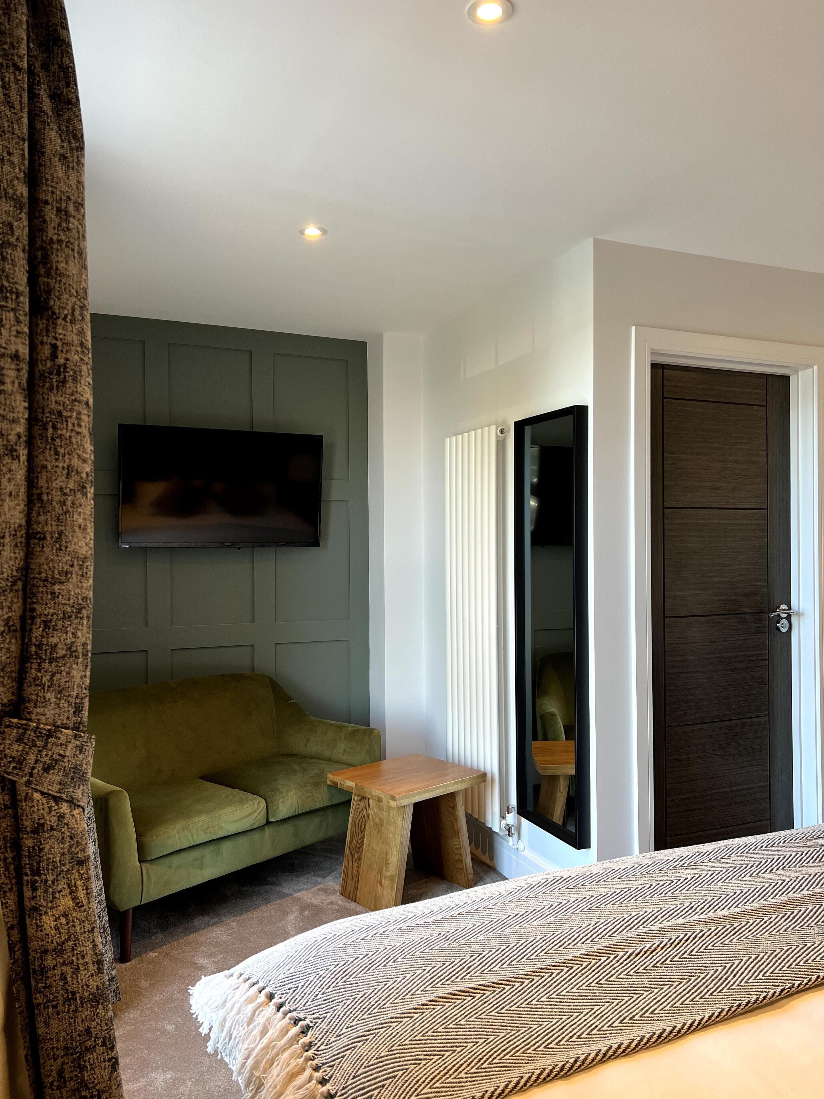 A modern bedroom with a green sofa, a wooden side table, a patterned throw, and a dark door.