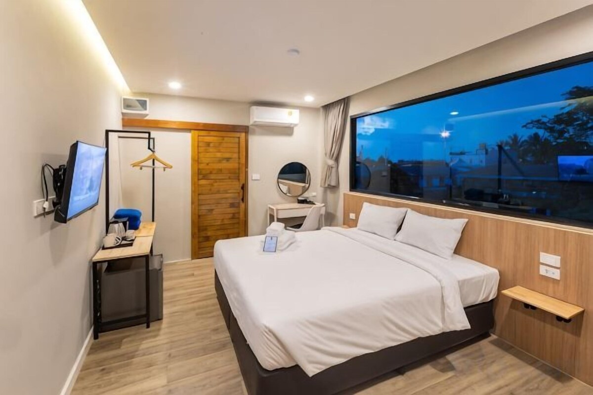 Une chambre d’hôtel moderne, dotée d’un grand lit, d’un bureau avec un ordinateur, d’une télévision et d’une fenêtre donnant sur la ville.