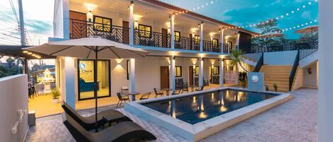 A hotel with a swimming pool, outdoor seating, and a two-story structure.