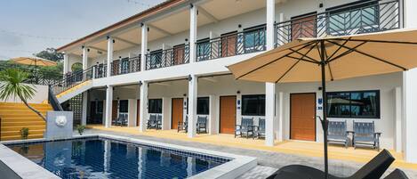 A hotel with a swimming pool, outdoor seating, and a covered balcony area.