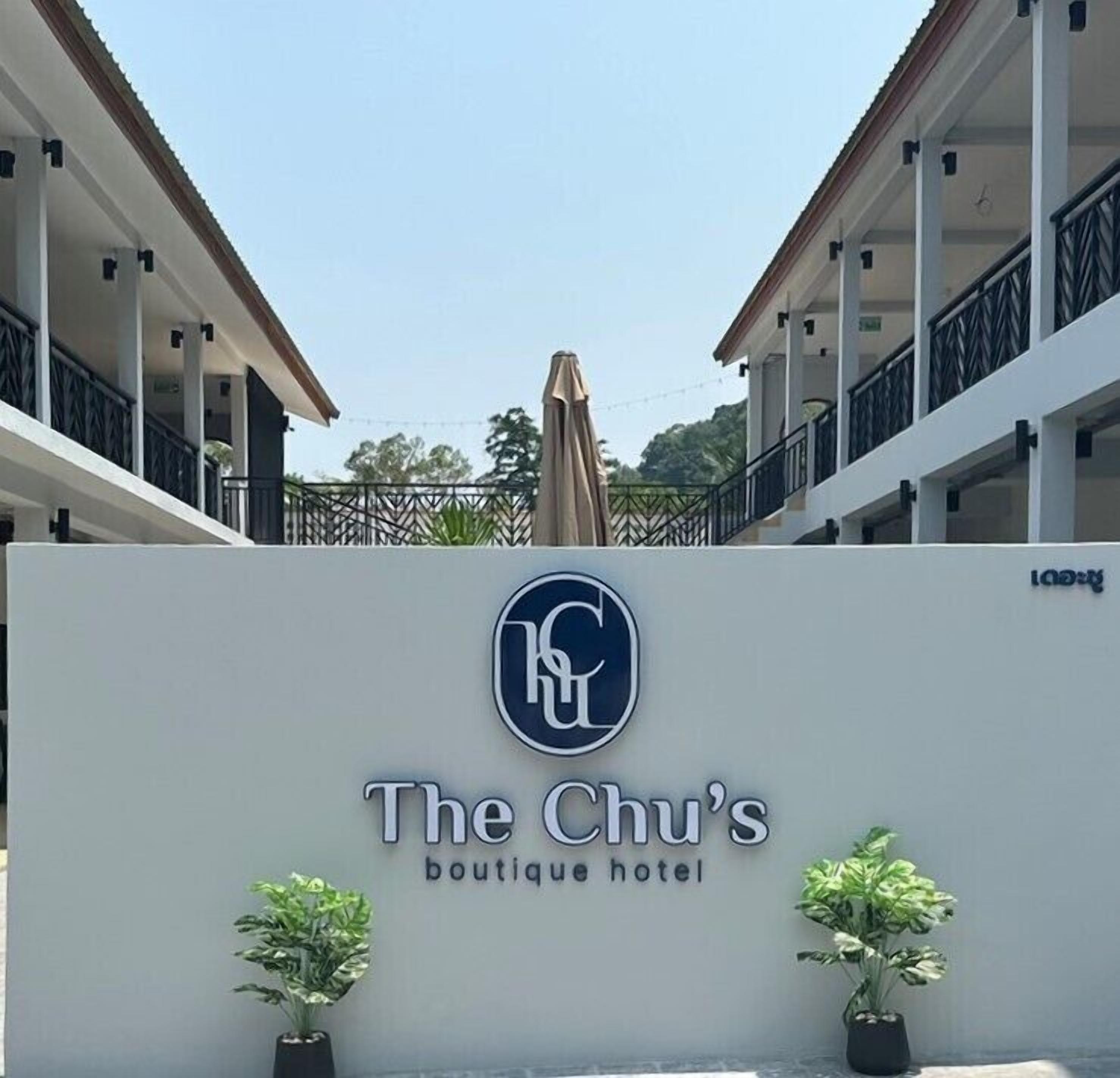 La entrada del hotel boutique Chu, con un letrero, plantas en macetas y vista del exterior del edificio.