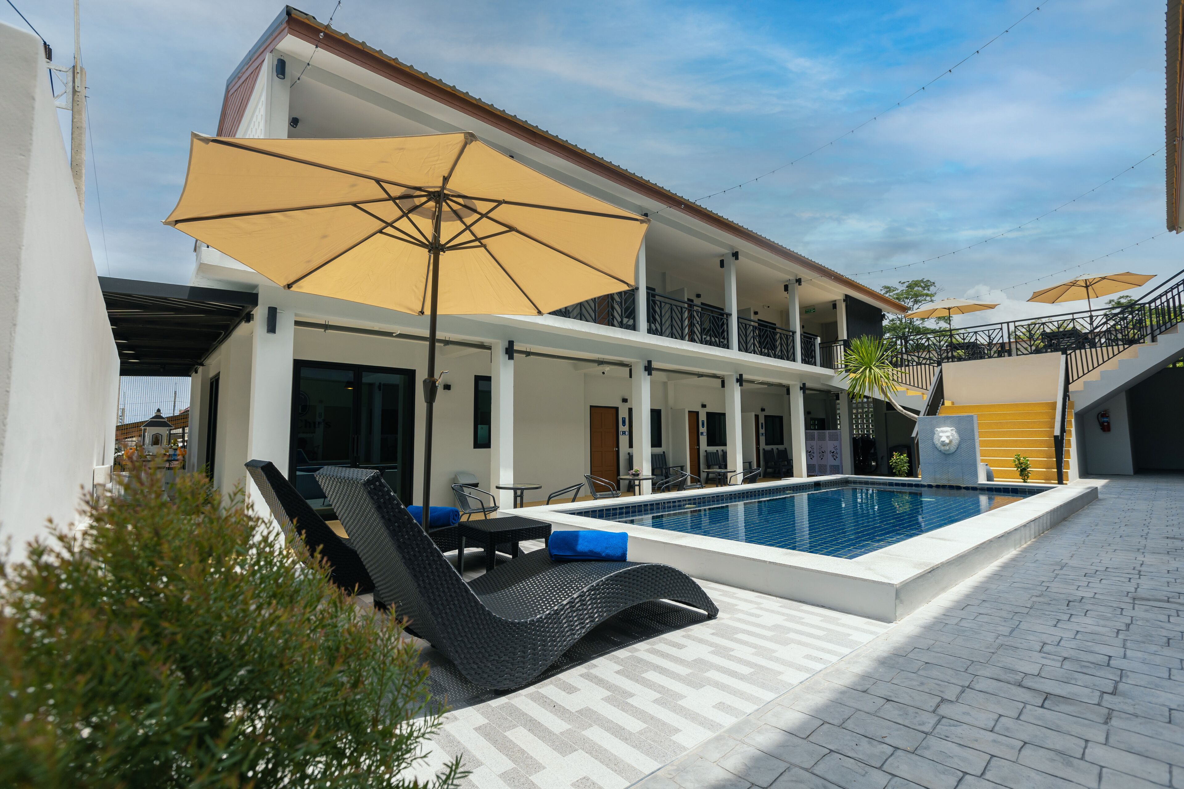 A pool area with lounge chairs and umbrellas, a covered seating area, and a staircase leading to an upper level.