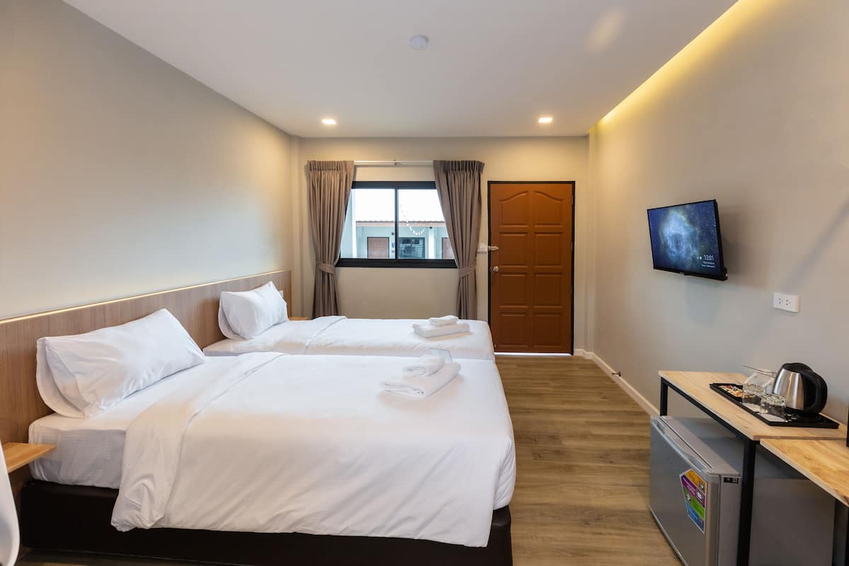 Habitación de hotel con dos camas, un televisor, un escritorio con hervidor y un refrigerador.