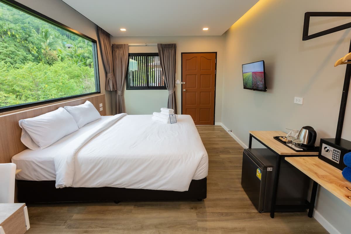 Una habitación de hotel con una cama, un escritorio con cafetera, un televisor y vistas a zonas verdes.