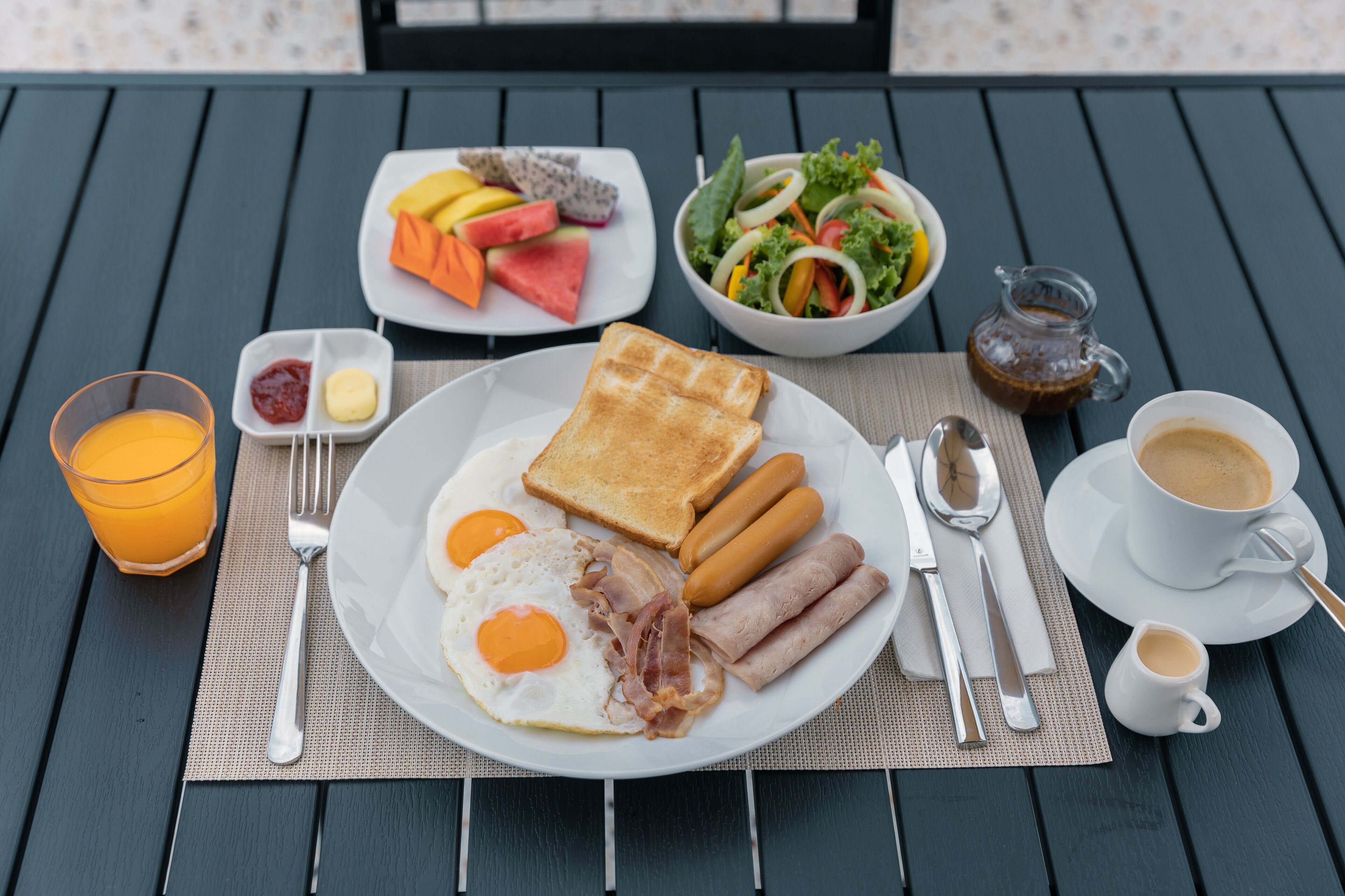 A breakfast plate with eggs, bacon, sausages, toast, and a side salad.