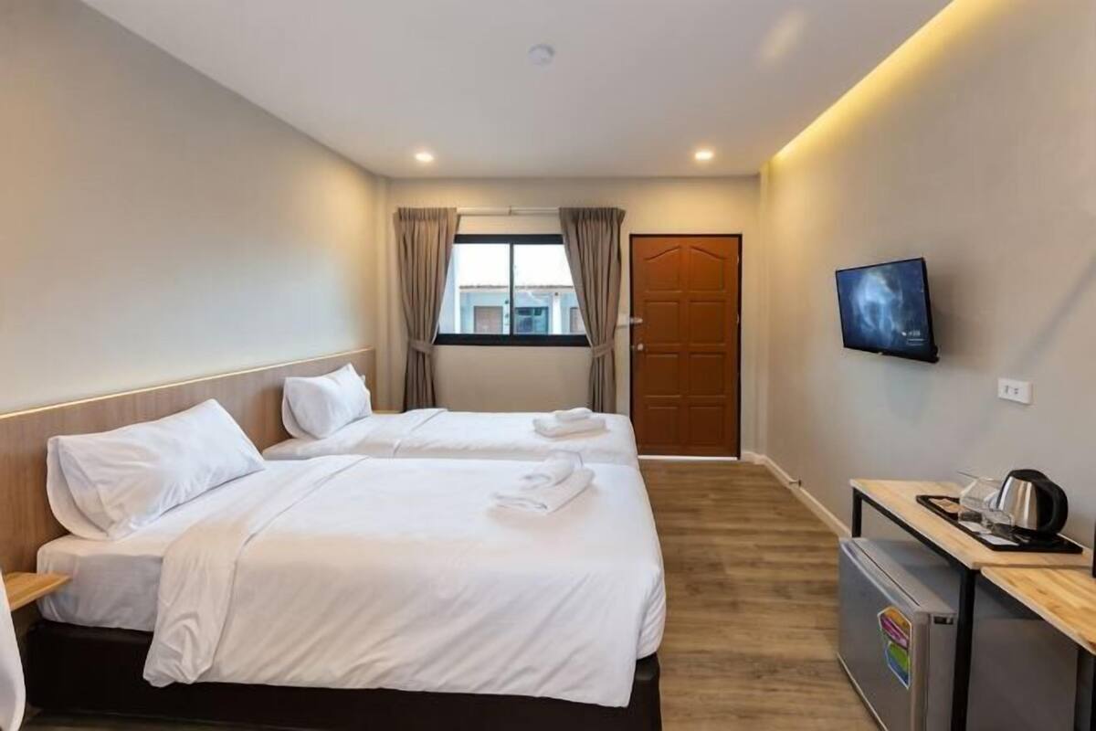 Una habitación de hotel con dos camas, un escritorio con computadora, televisión y una puerta.