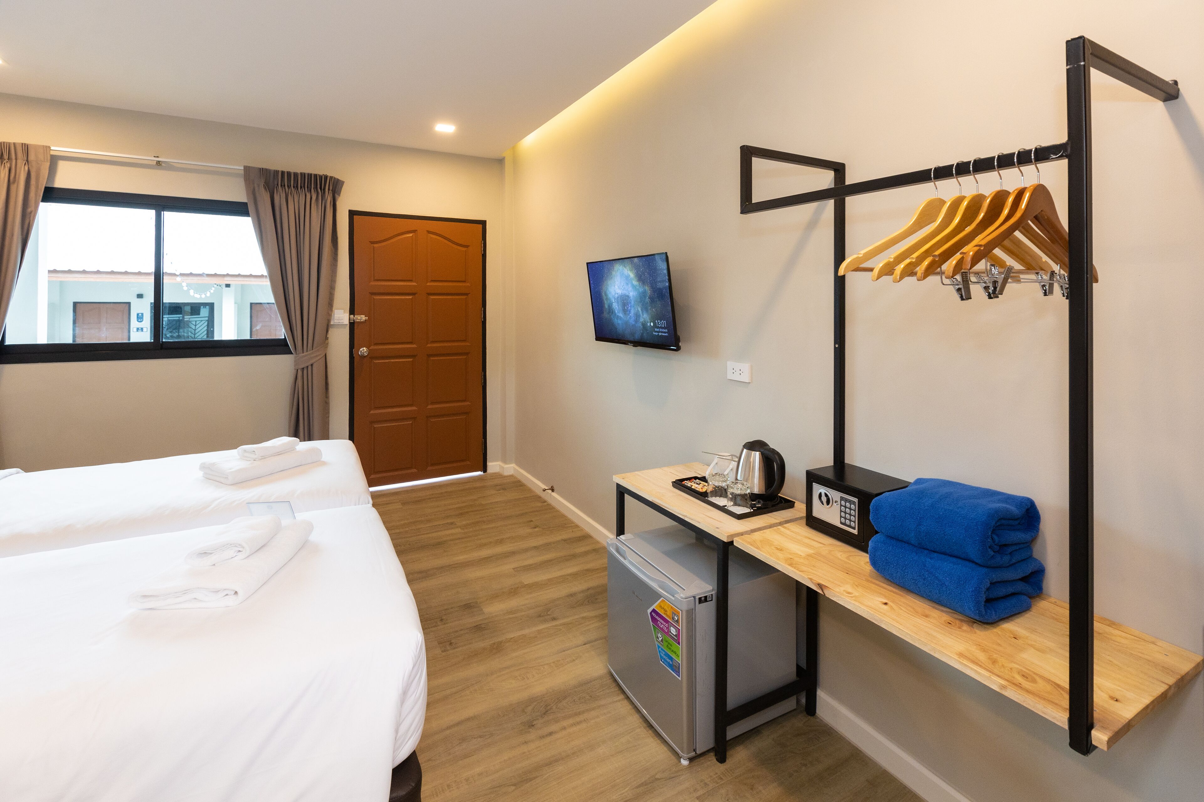 A hotel room with two beds, a desk with a kettle, a TV, and a coat rack.