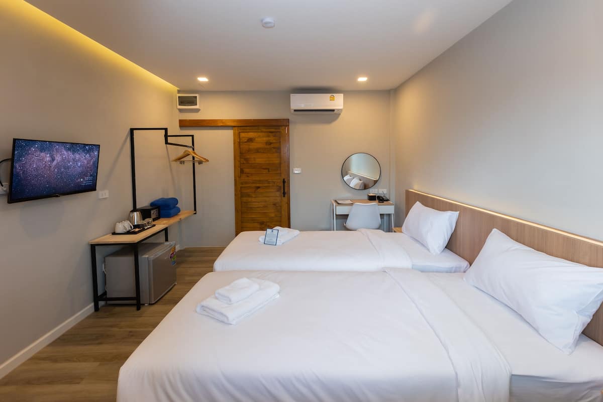 Habitación de hotel con dos camas, televisión, escritorio, espejo y aire acondicionado.