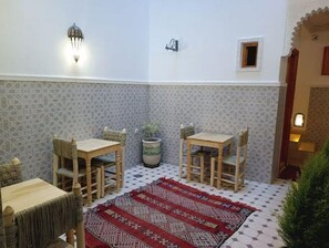 A courtyard with two wooden tables and chairs, a patterned rug, and a potted plant.