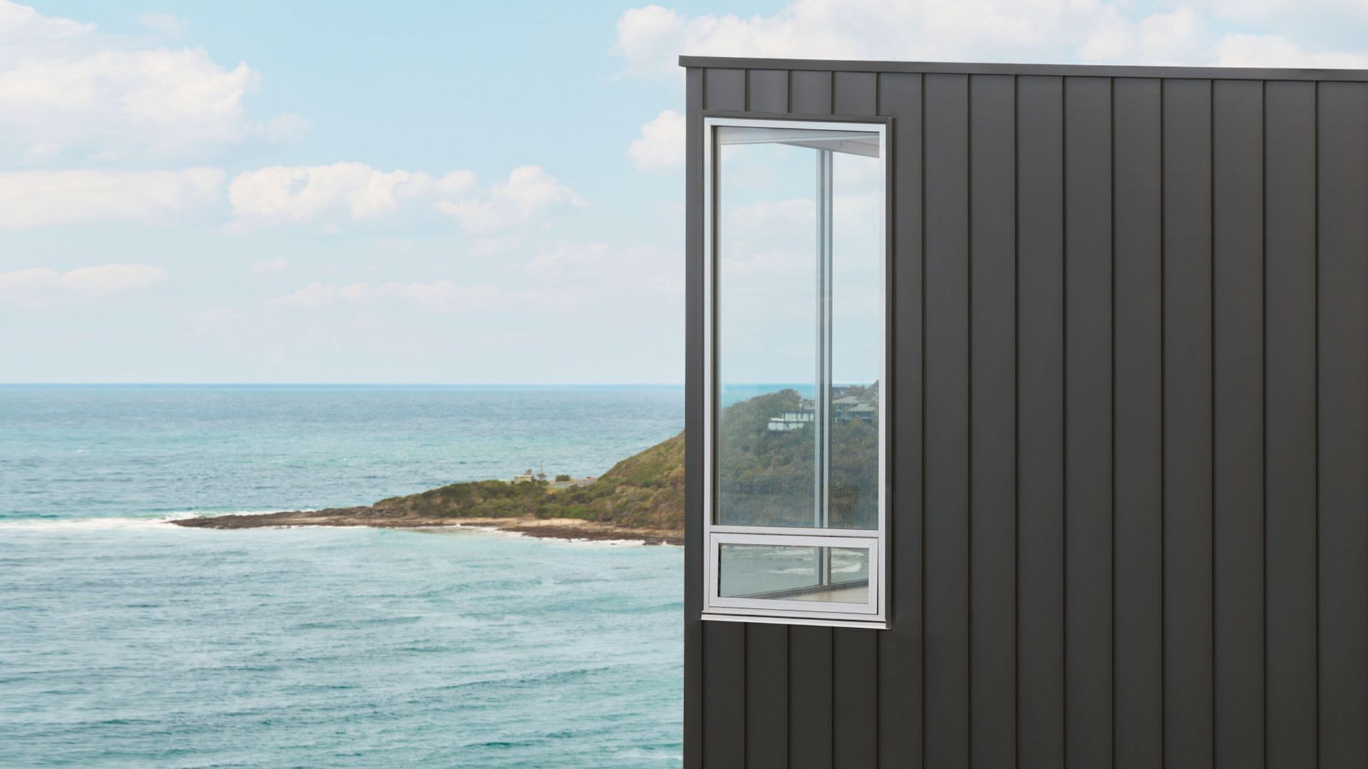 A coastal building with a large window offering a view of the ocean and a distant hill.