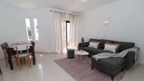 Un salon avec un canapé, une table à manger avec des chaises, une petite table ronde avec une bougie, et une vue par la fenêtre.