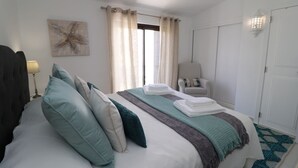 Un lit bien fait, avec des oreillers, une chaise, une lampe et une œuvre d’art représentant une étoile de mer accrochée au mur.